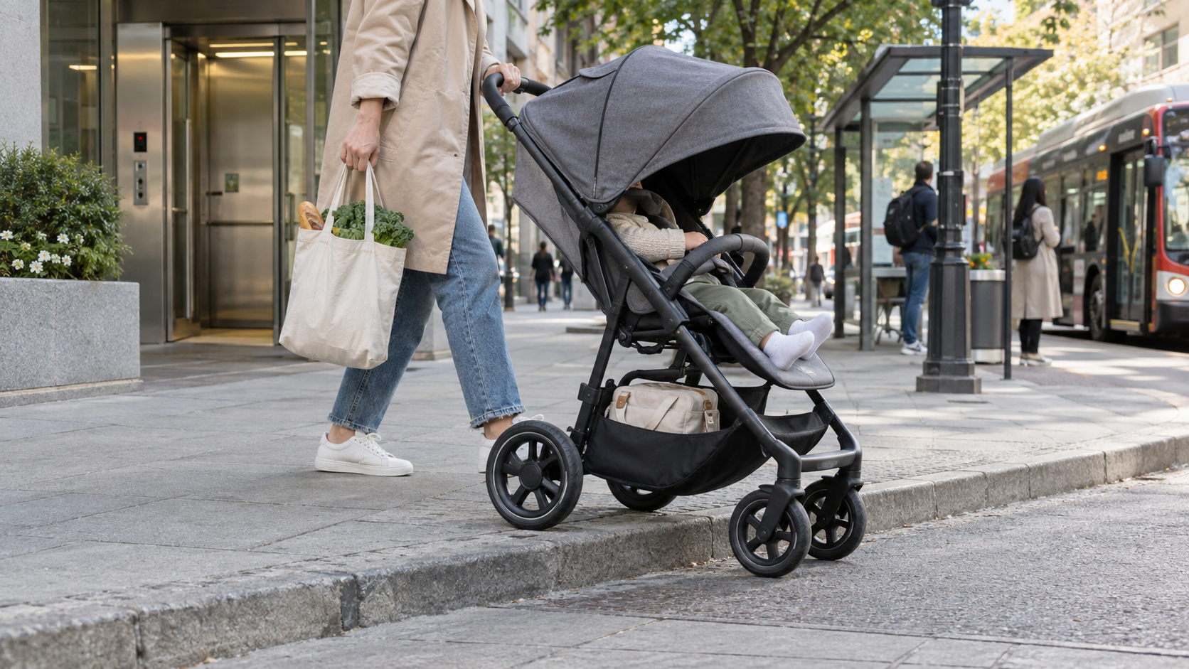 Parent pushing a stroller over a curb with a grocery tote and diaper bag during an urban outing.